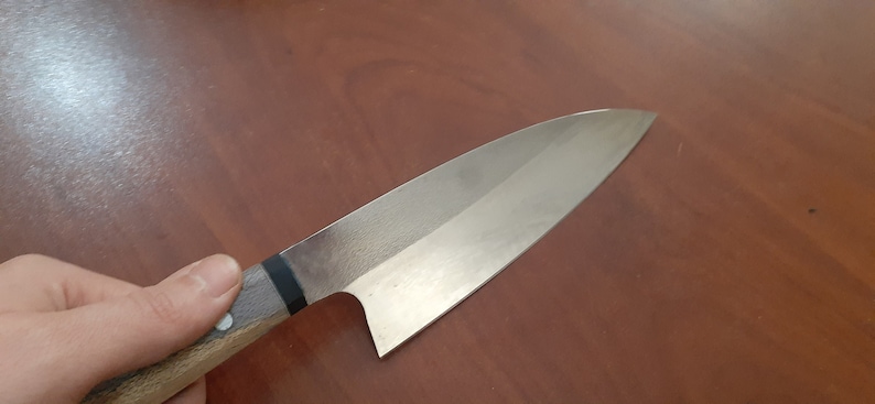 May include: A silver chef's knife with a wooden handle. The knife has a black stripe on the handle.