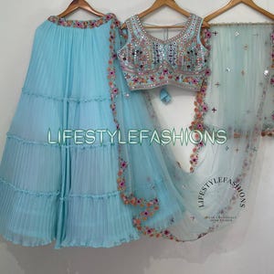 May include: A light blue layered skirt with a matching light blue sheer dupatta. The skirt has a ruffled hem and the dupatta features floral embroidery. A light blue embroidered blouse with mirror work is also included.