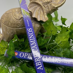 May include: Two packs of HEM incense sticks, one with the scent "Abre Caminos" and the other with the scent "Open Roads". Both packs are blue with white text and a gold HEM logo.