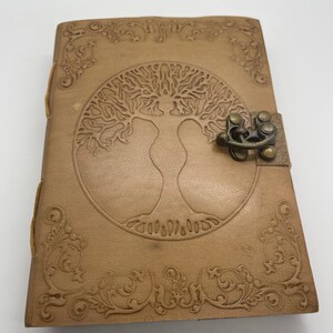 May include: A brown leather journal with a tree of life design embossed on the front cover. The journal has a metal clasp closure and decorative floral accents around the edges.