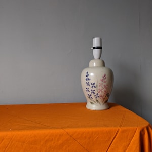 May include: A white ceramic table lamp with a floral design. The lamp has a white shade and a white base with a floral pattern in shades of pink, blue, and green.