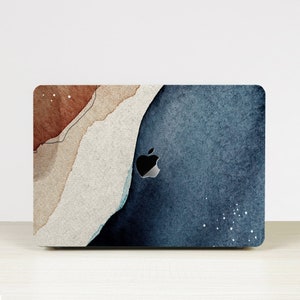 Könnte beinhalten: Laptop-Skin mit einem abstrakten Aquarelldesign. Das Design zeigt eine Mischung aus Braun-, Beige- und Blautönen mit strukturiertem Aussehen. Das Apple-Logo ist sichtbar. Die Gesamtästhetik ist künstlerisch und modern.