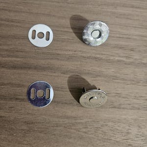 May include: Four silver magnetic snap closures for bags or crafts. Two are flat with holes, and two are round with a textured pattern. The magnetic closures are designed to be sewn into fabric.
