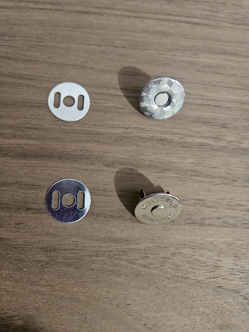 May include: Four silver magnetic snap closures for bags or crafts. Two are flat with holes, and two are round with a textured pattern. The magnetic closures are designed to be sewn into fabric.