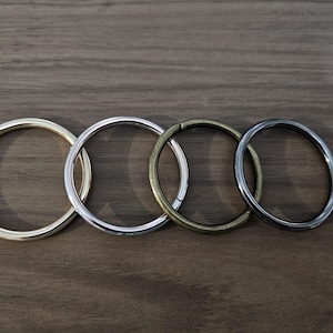 May include: Four metal rings in different sizes and finishes: gold, silver, brass, and black. The rings are arranged in a row from largest to smallest.