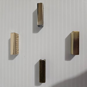 May include: Four metal rectangular slider buckles in different finishes: gold, silver, brass, and a gold buckle with a textured surface.