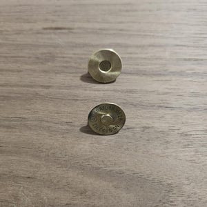 May include: Two brass-colored magnetic snap closures. One is a solid disc with a central hole, the other has stamped text including "NO.883313". These closures are likely for bags or other craft projects.