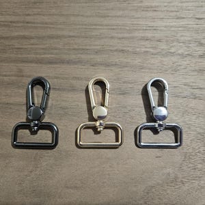 May include: Three metal clasps in black, gold, and silver. Each clasp has a rectangular loop and a hook.