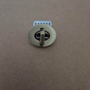 May include: A gold-toned metal clasp with a hook and a small, round, decorative plate. The plate has a raised, circular design in the center.