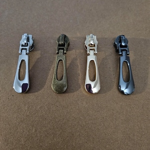 May include: Four zipper pulls in different finishes: black, silver, antique brass, and gold.