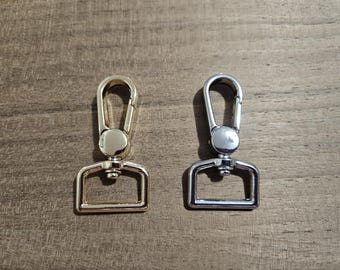 Puede incluir: Dos cierres metálicos, uno dorado y otro plateado, con un bucle rectangular y un gancho. Los cierres se utilizan comúnmente para sujetar correas o cadenas a bolsos, carteras u otros accesorios.