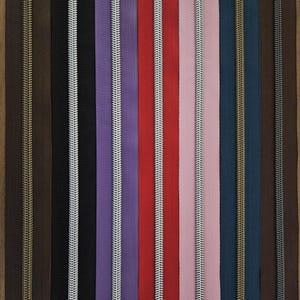 Puede incluir: Una colecci&oacute;n de cremalleras coloridas en varios tonos, incluyendo marr&oacute;n, negro, morado, rojo, rosa y azul. Cada cremallera tiene un tirador de metal contrastante. Las cremalleras est&aacute;n dispuestas verticalmente.