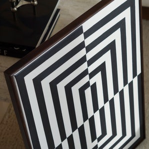 Pu&ograve; includere: Motivo geometrico bianco e nero incorniciato in una cornice di legno marrone scuro. Il motivo &egrave; composto da linee orizzontali e verticali che creano una serie di quadrati e rettangoli.