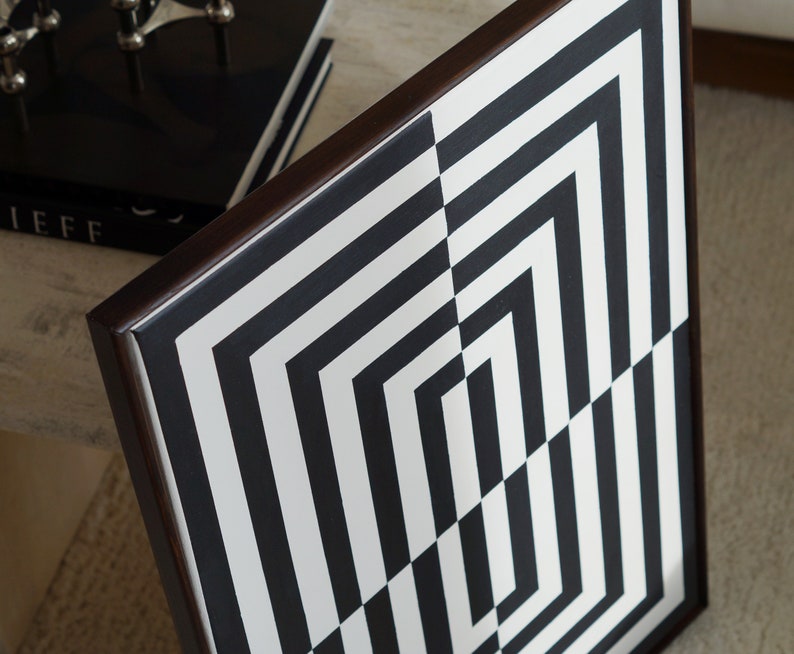 Pu&ograve; includere: Motivo geometrico bianco e nero incorniciato in una cornice di legno marrone scuro. Il motivo &egrave; composto da linee orizzontali e verticali che creano una serie di quadrati e rettangoli.