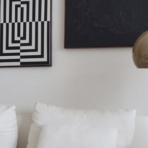 Pu&ograve; includere: Un divano bianco con due cuscini bianchi e un'opera d'arte geometrica in bianco e nero appesa al muro sopra.