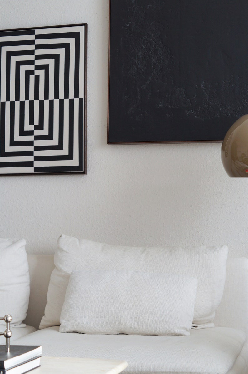 Pu&ograve; includere: Un divano bianco con due cuscini bianchi e un'opera d'arte geometrica in bianco e nero appesa al muro sopra.