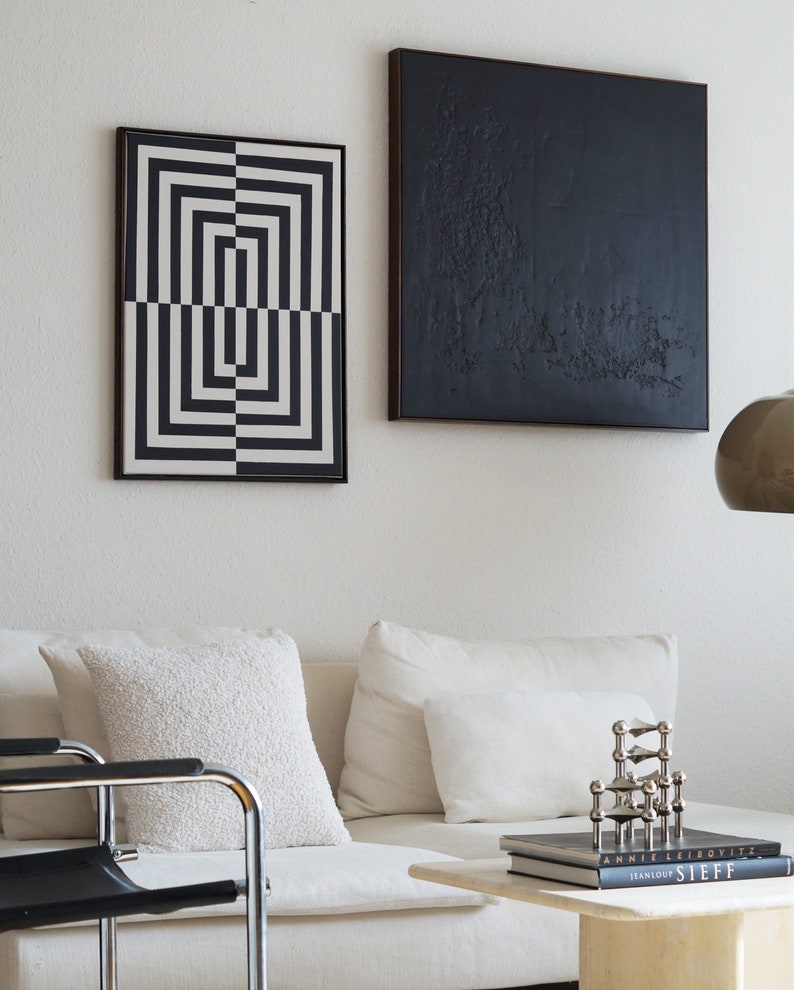 Pu&ograve; includere: Un divano bianco con due cuscini bianchi e un'opera d'arte incorniciata con stampa geometrica in bianco e nero appesa al muro sopra. Un'opera d'arte incorniciata in bianco e nero con una superficie nera testurizzata &egrave; appesa al muro a destra del divano. Una scultura in metallo argentato &egrave; su un tavolino da caff&egrave; bianco con due libri impilati sotto. I libri sono intitolati "Annie Leibovitz" e "Jeanloup Sieff".