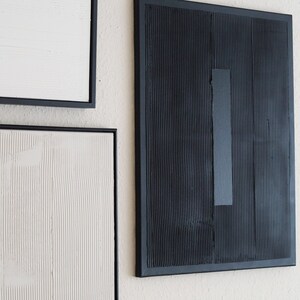 Pode incluir: Arte de parede abstrata com superf&iacute;cies texturizadas e molduras pretas. A obra de arte inclui uma pe&ccedil;a retangular preta com um detalhe vertical cinza e outras pe&ccedil;as emolduradas em branco e branco-sujo.