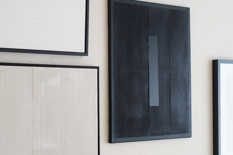 Pode incluir: Arte de parede abstrata com superf&iacute;cies texturizadas e molduras pretas. A obra de arte inclui uma pe&ccedil;a retangular preta com um detalhe vertical cinza e outras pe&ccedil;as emolduradas em branco e branco-sujo.