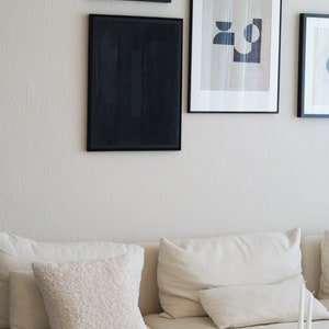 Pode incluir: Uma cena de sala de estar com arte emoldurada e um sof&aacute; creme com almofadas. A arte de parede inclui uma pe&ccedil;a abstrata emoldurada em preto e outras impress&otilde;es emolduradas. Uma almofada texturizada e velas s&atilde;o vis&iacute;veis.