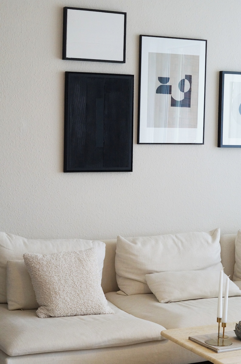 Pode incluir: Uma cena de sala de estar com arte emoldurada e um sof&aacute; creme com almofadas. A arte de parede inclui uma pe&ccedil;a abstrata emoldurada em preto e outras impress&otilde;es emolduradas. Uma almofada texturizada e velas s&atilde;o vis&iacute;veis.