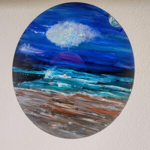 May include: A painted vinyl record with a seascape scene. The record features a blue sky with a white cloud, a dark blue ocean with white waves, and a brown sandy beach.