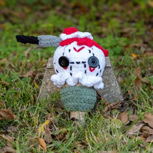 May include: A crocheted plush toy shaped like an ice cream cone with a white and red hat and a green cone. The toy has black button eyes and a stitched-on mouth.