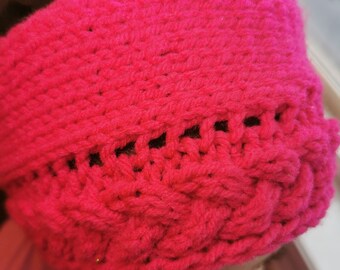 Könnte beinhalten: Ein pinkfarbenes Strickband mit einem Zopfmuster. Das Stirnband ist aus weichem Garn gefertigt und hat eine bequeme Passform.