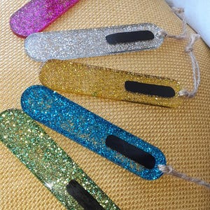 May include: Five colourful glitter bookmarks with black chalkboard inserts and twine string. The bookmarks are pink, silver, gold, blue, and green.