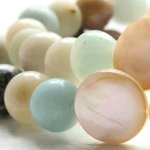 May include: A close-up of a strand of beads made from various materials, including white, cream, light blue, and pink. The beads are round and smooth, and they are arranged in a random pattern.