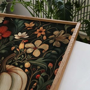 Peut inclure: Une impression d'art encadr&eacute;e avec un motif floral et de citrouille d&eacute;taill&eacute;. L'&oelig;uvre pr&eacute;sente une vari&eacute;t&eacute; de fleurs orange, blanches et jaunes, sur un fond vert fonc&eacute;. Le cadre est en bois clair.