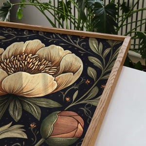 May include: A framed print with a floral pattern featuring large, light brown flowers with orange centers and green leaves on a dark blue background.