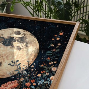Pode incluir: Uma impress&atilde;o emoldurada de uma lua com acabamento met&aacute;lico dourado, cercada por um fundo azul escuro com estrelas brancas e um grupo de flores coloridas em primeiro plano.