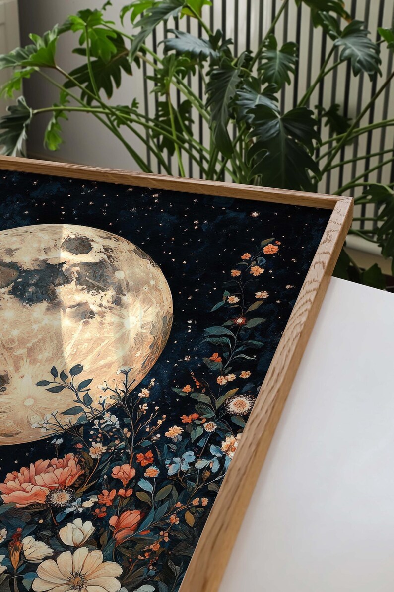 Pode incluir: Uma impress&atilde;o emoldurada de uma lua com acabamento met&aacute;lico dourado, cercada por um fundo azul escuro com estrelas brancas e um grupo de flores coloridas em primeiro plano.