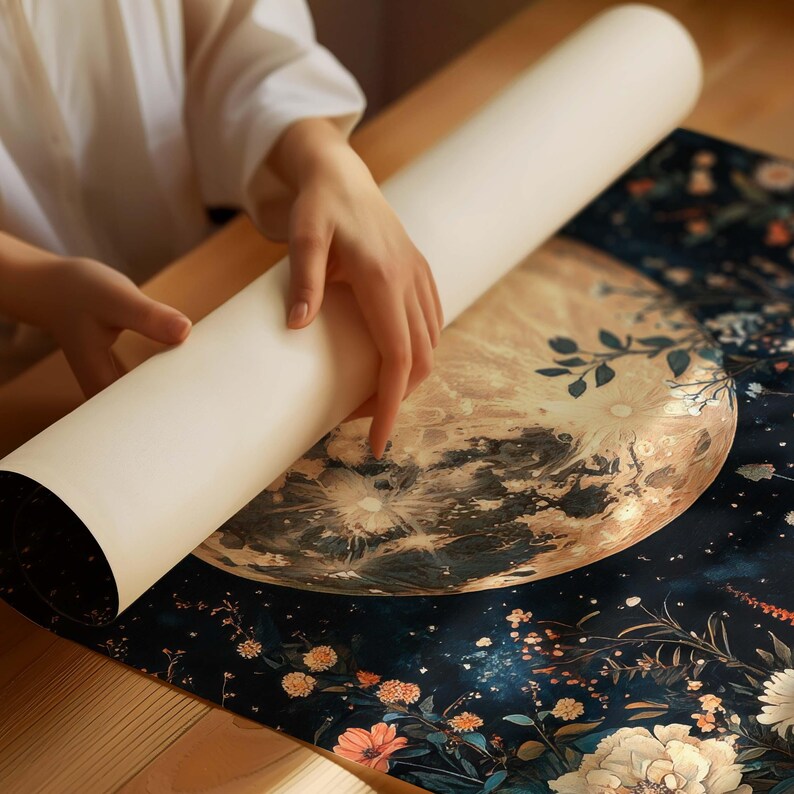 Pode incluir: Um p&ocirc;ster enrolado com um fundo azul escuro que apresenta uma grande ilustra&ccedil;&atilde;o detalhada de uma lua com um design floral. A lua &eacute; de cor amarelo claro e marrom com um brilho branco no centro. O design floral est&aacute; em tons de rosa, branco e verde.