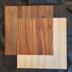 Puede incluir: Una tabla de cortar de madera con un dise&ntilde;o &uacute;nico. La tabla est&aacute; hecha de tres tipos diferentes de madera: nogal, arce y cerezo. El nogal es de color marr&oacute;n oscuro, el arce es de color marr&oacute;n claro y el cerezo es de color marr&oacute;n rojizo.