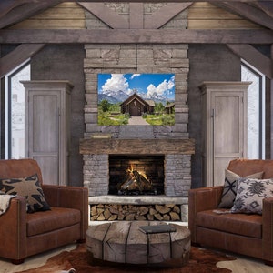 May include: A rustic living room with a stone fireplace, two brown leather armchairs, a wooden coffee table, and a framed landscape photograph of a wooden church in a mountain valley.
