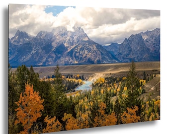 Könnte beinhalten: Eine Landschaftsaufnahme mit einem gewundenen blauen Fluss, der durch ein Tal mit immergrünen und goldenen Herbstbäumen fließt, vor einer Kulisse aus hoch aufragenden, schroffen Berggipfeln, die teilweise von weißen Wolken verdeckt sind.