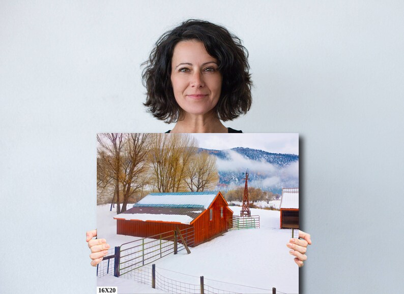 May include: A red barn with a white roof and a snow-covered field in front of it. The barn is surrounded by a wooden fence and there are trees in the background. The text "16X20" is printed in the bottom left corner of the image.