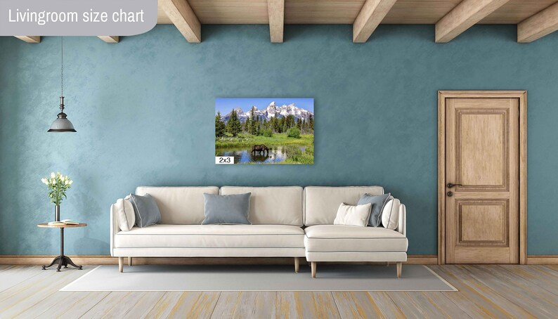 Op de afbeelding: Een witte bank met blauwe kussens in een woonkamer met een groot canvasprint van een berglandschap erboven. De canvasprint is in de linkerbenedenhoek met "2x3" gelabeld.