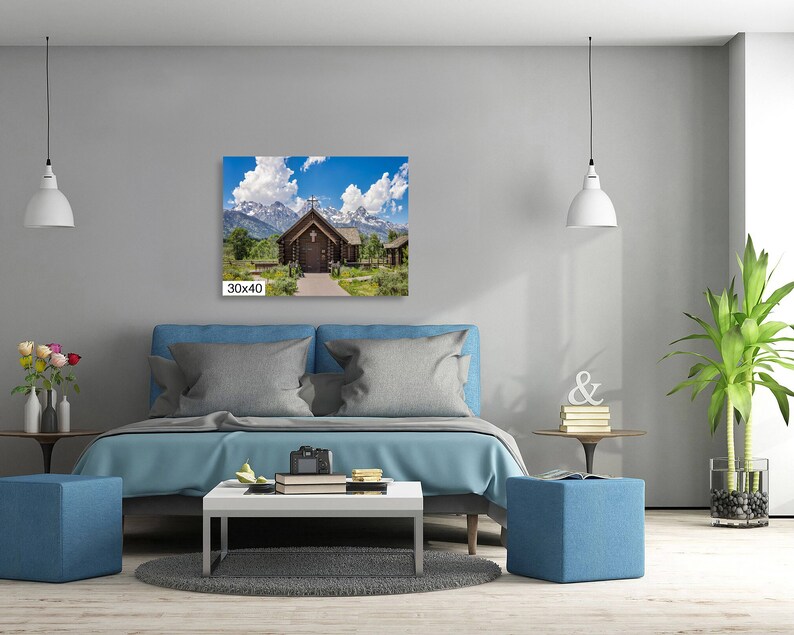 May include: A photograph of a wooden chapel with a cross on the roof, surrounded by green trees and snow-capped mountains in the background. The chapel is located in a field with a path leading to the front door. The sky is blue with white clouds.