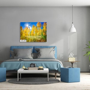 Może przedstawiać: Wydruk na pł&oacute;tnie o wymiarach 76x102 cm przedstawia jesienny krajobraz. Grafika przedstawia wysokie drzewa z ż&oacute;łtymi liśćmi na tle błękitnego nieba i jasnego słońca. Tekst jest widoczny na wydruku.