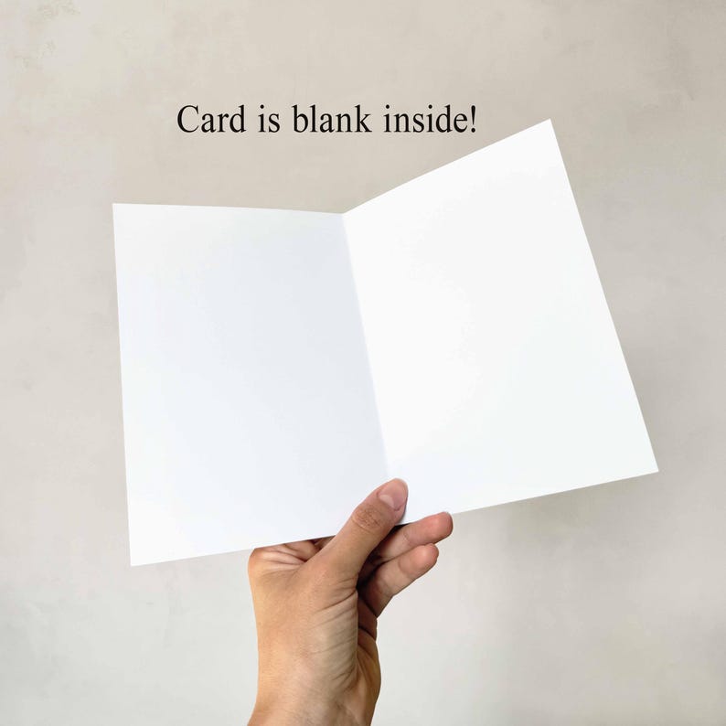 May include: A blank white greeting card, held open to display the inside. The card is open, revealing two blank white pages. The text "Card is blank inside!" is printed above the card.