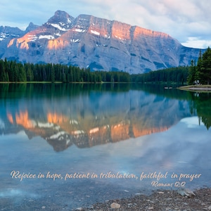 Può includere: Un paesaggio panoramico con una catena montuosa riflessa in un lago calmo. Le cime delle montagne sono illuminate dalla luce del sole. L'immagine include il testo: "Rallegratevi nella speranza, siate pazienti nella tribolazione, perseveranti nella preghiera Romani 12:12."