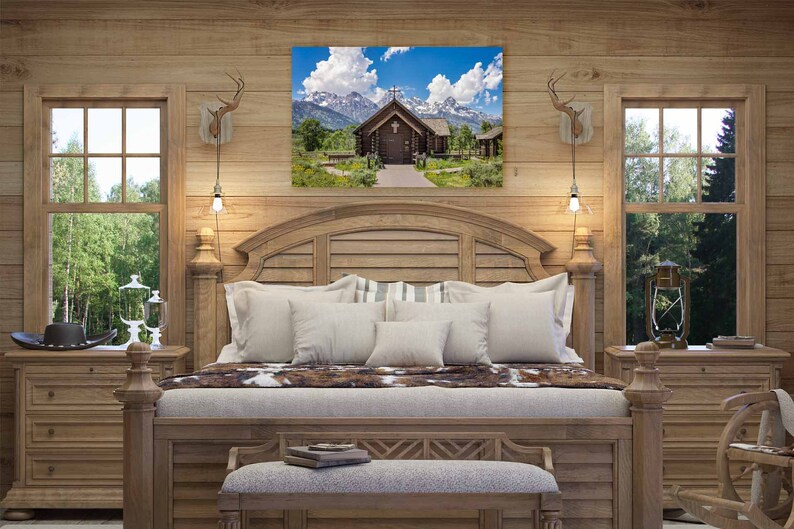 May include: A rustic wooden bedroom with a large bed, two nightstands, and a framed picture of a wooden chapel in the mountains. The bed has a white comforter and a brown and white cowhide throw. The nightstands have drawers and lamps. The picture is above the headboard.