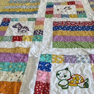 May include: A white quilted baby blanket with a patchwork design featuring various colorful fabrics. The blanket has embroidered animal designs, including a zebra, a horse, and a turtle.