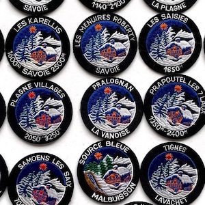 May include: A collection of 20 embroidered patches featuring various French ski resorts. Each patch is circular and features a blue background with white snow-capped mountains, a small cabin, and the resort name in white text. The patches also include the resort's altitude in metres.