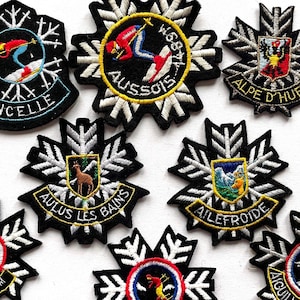 May include: Nine embroidered patches with snowflake designs. Each patch features a different ski resort name and logo, including Ancelle, Aussois, Alpe d'Huez, Aulus les Bains, Ailefroide, and Aigulles 14/04.
