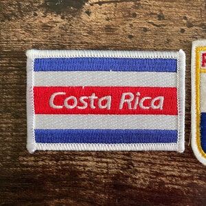 Pode incluir: Dois patches bordados. Um patch retangular apresenta a bandeira da Costa Rica com o texto "Costa Rica". O outro patch tem formato de escudo, exibindo a bandeira do Panamá com a palavra "PANAMA" no topo.