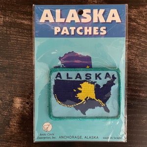 Peut inclure: Un écusson rectangulaire de l'Alaska dans une pochette en plastique. L'écusson représente une carte de l'Alaska en jaune et un fond bleu foncé, avec le mot "ALASKA" au-dessus. L'emballage indique "ALASKA PATCHES".